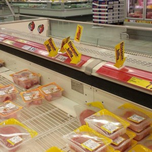 A large cooler for food and meat in a german supermarket is nearly empty. Above it is an advertising in yellow that marks it as cheap.